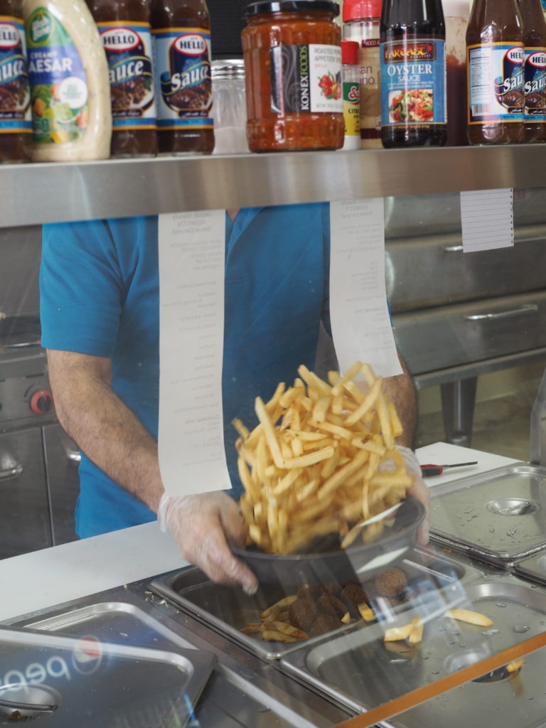 A man in a blue shirt shakes a tray of french fries to season them