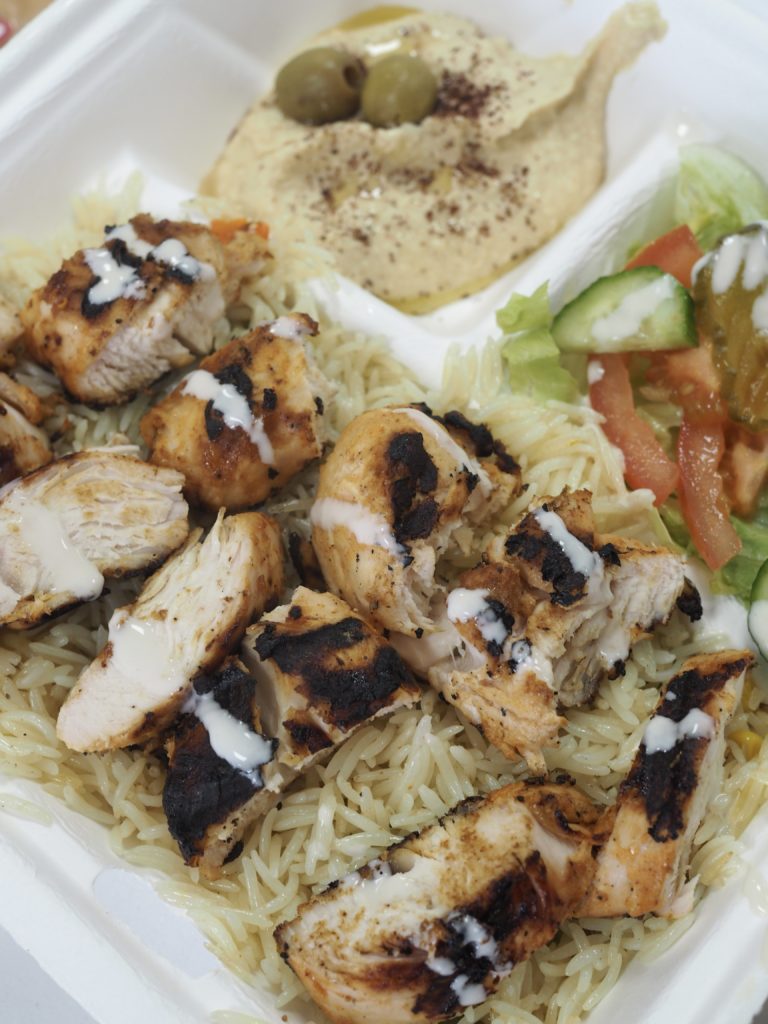 Closeup of a plate of grilled chicken, rice and hummus