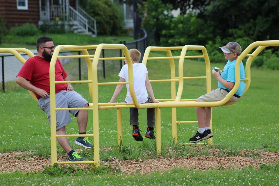 A Behavioral Health Providers sits with two boys on a piece of playground equipment
