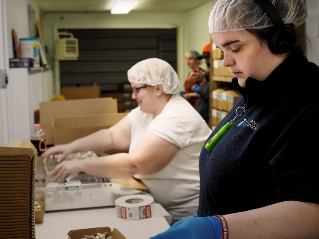 Two white women in hair nets weigh mushrooms