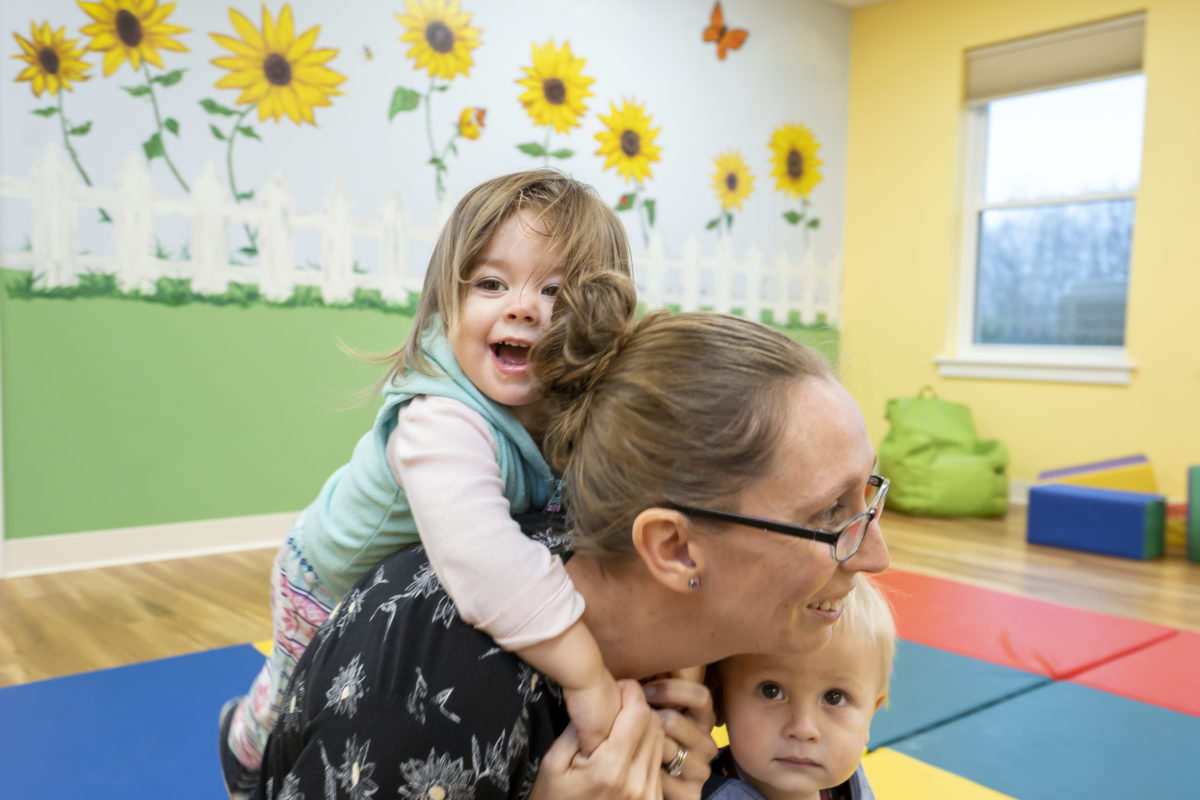A daycare worker carries a smiling child on her back