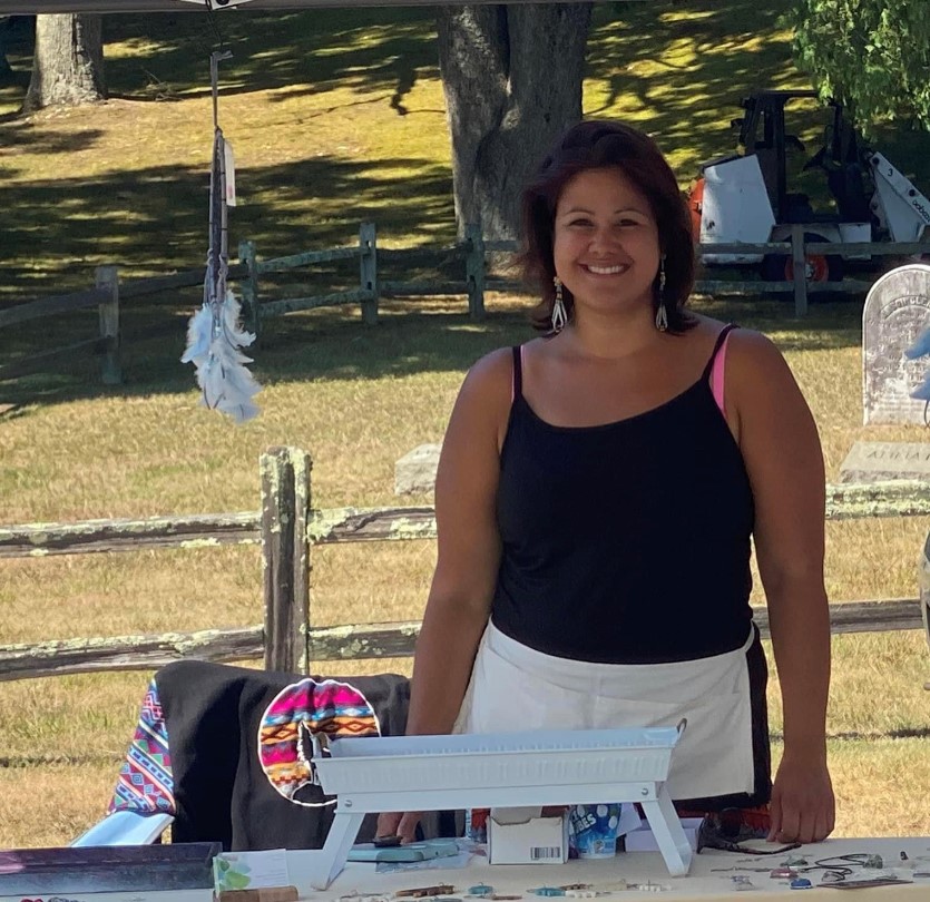 A smiling Passamaquoddy Native American woman standing in front of a craft fair booth
