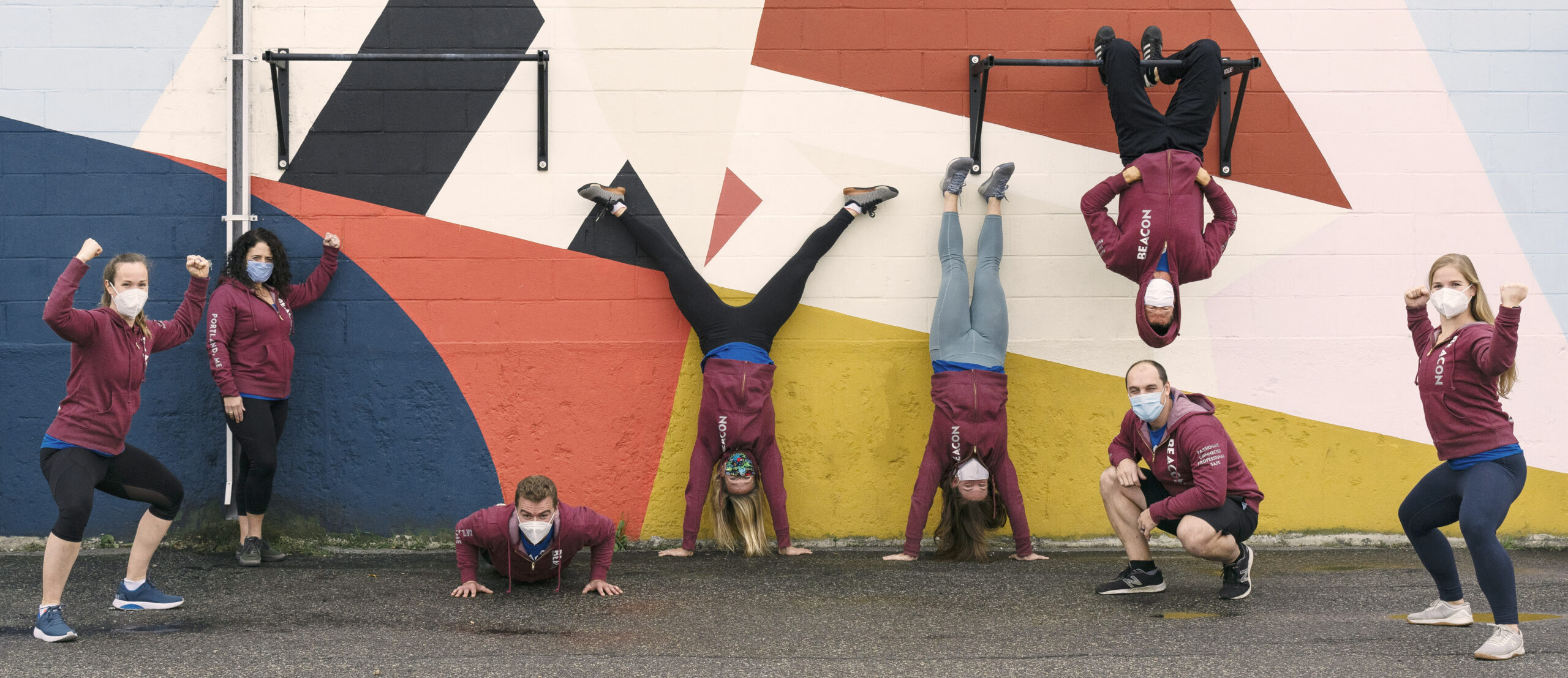 The employees of a fitness center, wearing medical masks, are doing handstands and pushups with enthusiasm