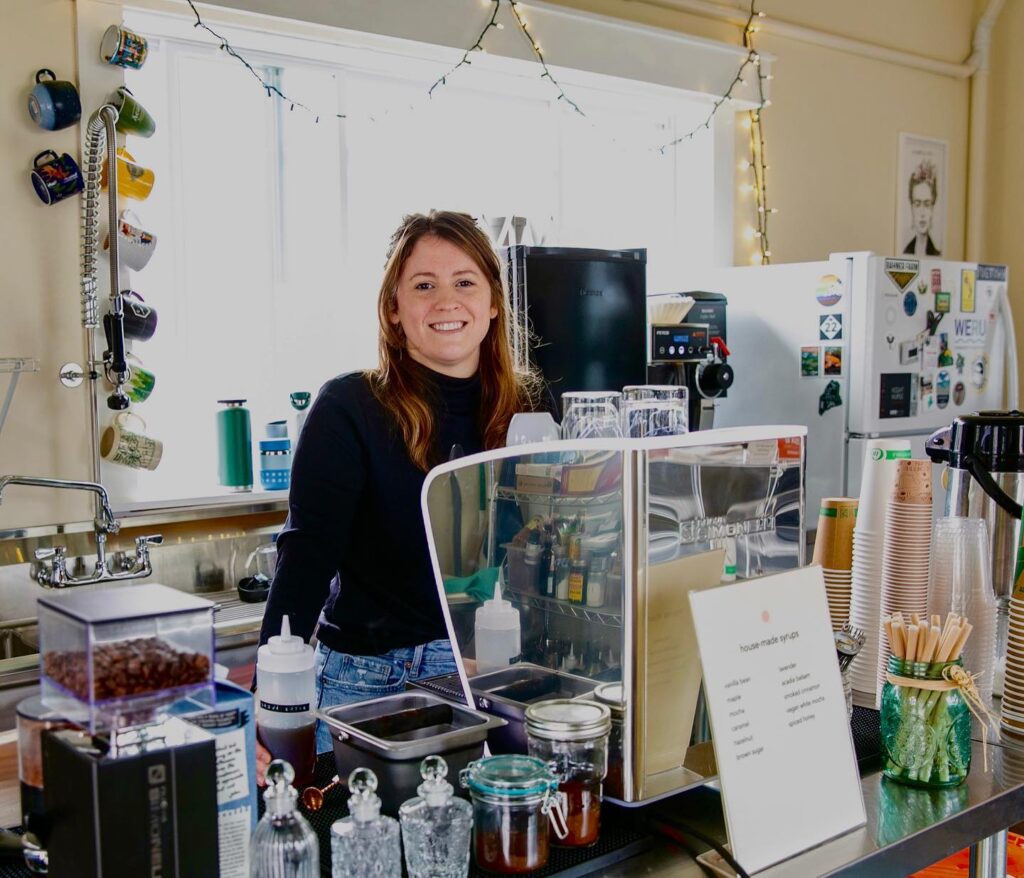 A young white woman stands behind the counter at a solar-powered coffee roastery.