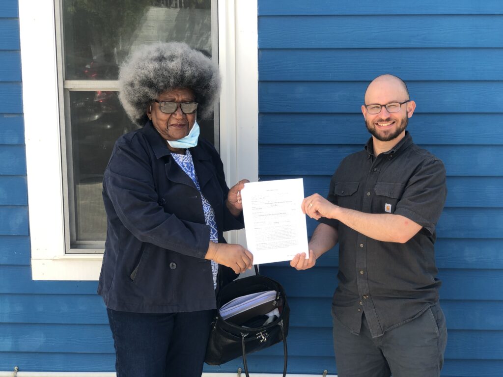 A black business woman smiles as a white man in glasses hands her a signed document